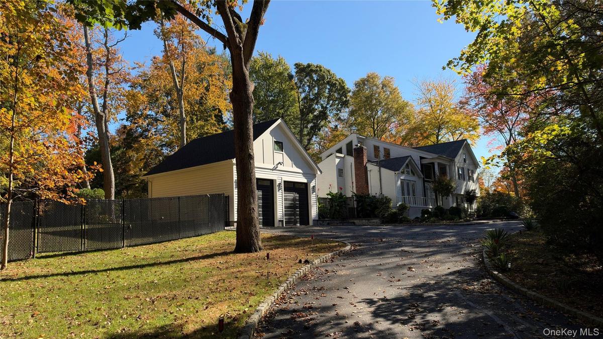 Multi-level residence with white siding and a brick chimney, featuring a detached two-car garage, asphalt driveway, and black chain-link fencing