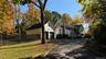 Multi-level residence with white siding and a brick chimney, featuring a detached two-car garage, asphalt driveway, and black chain-link fencing