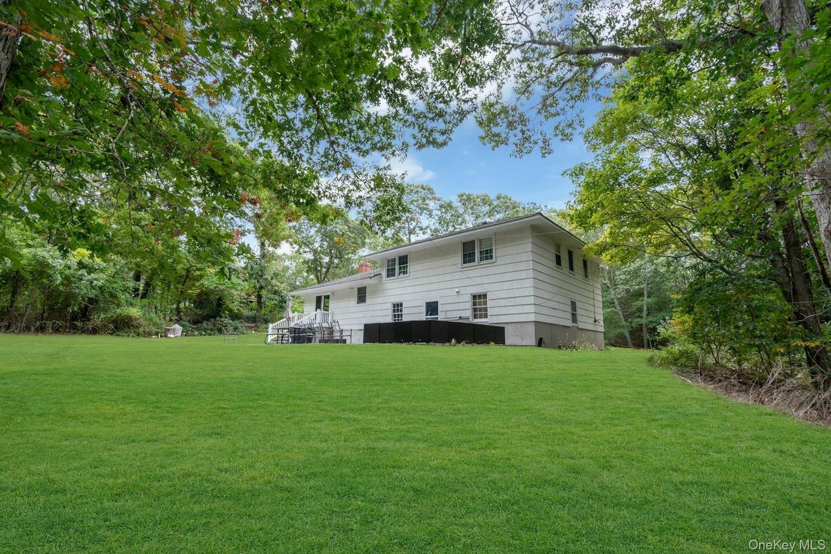 Two-story residence with white horizontal siding, stone foundation, multi-pane windows, and extensive surrounding mature tree canopy situated on a spa