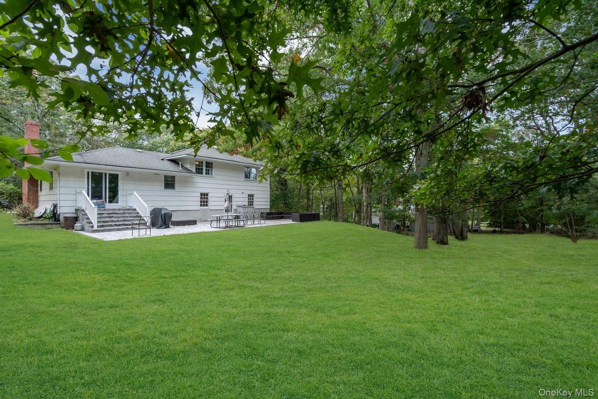 Expansive rear lawn with mature trees, stone patio, and brick chimney