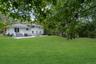 Expansive rear lawn with mature trees, stone patio, and brick chimney