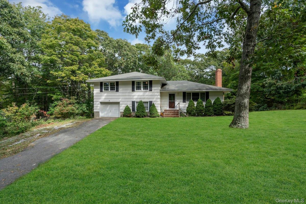 Split-level exterior featuring white siding, black shutters, an integrated garage, brick chimney, and concrete stairs