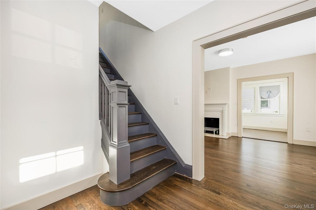 Staircase featuring dark-toned wood treads and painted balustrade with a prominent newel post, finished with dark-toned wood flooring and a classic fi