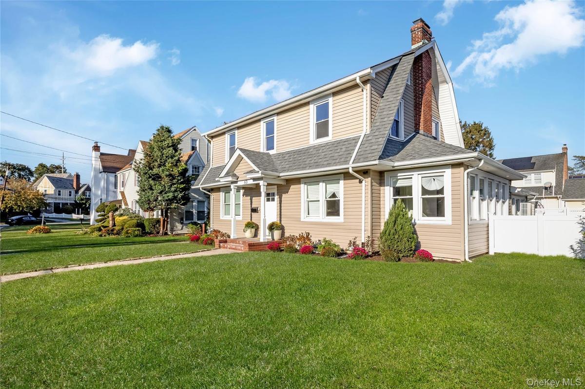 Colonial exterior featuring vinyl siding, an exposed brick chimney, a covered entryway with columns, and asphalt shingle roofing. Grass is virtually e