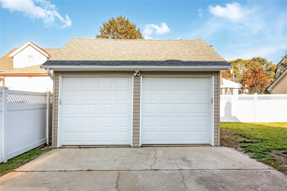 Detached two-car garage with electric featuring dual paneled overhead doors, vinyl siding, a shingled roof, and an exterior concrete apron, enclosed b