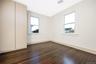 Bedroom featuring dark wood-finish flooring, neutral wall tones, dual windows with white trim, and a floor-to-ceiling built-in storage cabinet