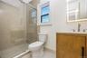 Full bathroom on first floor. Stall shower with glass enclosure and neutral tile surround, vanity with stone-surface countertop, and backlit wall mirr