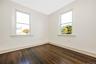 Bedroom with dark-toned wood-finish flooring paired with neutral-colored walls, featuring dual double-hung windows with white trim