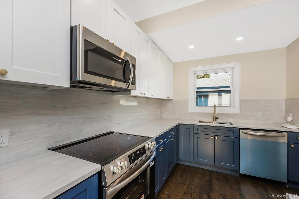 Eat in kitchen featuring two-tone navy and white shaker cabinetry, quartz countertops, stainless steel appliances, a center island, and wood-finish fl