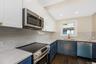 Eat in kitchen featuring two-tone navy and white shaker cabinetry, quartz countertops, stainless steel appliances, a center island, and wood-finish fl