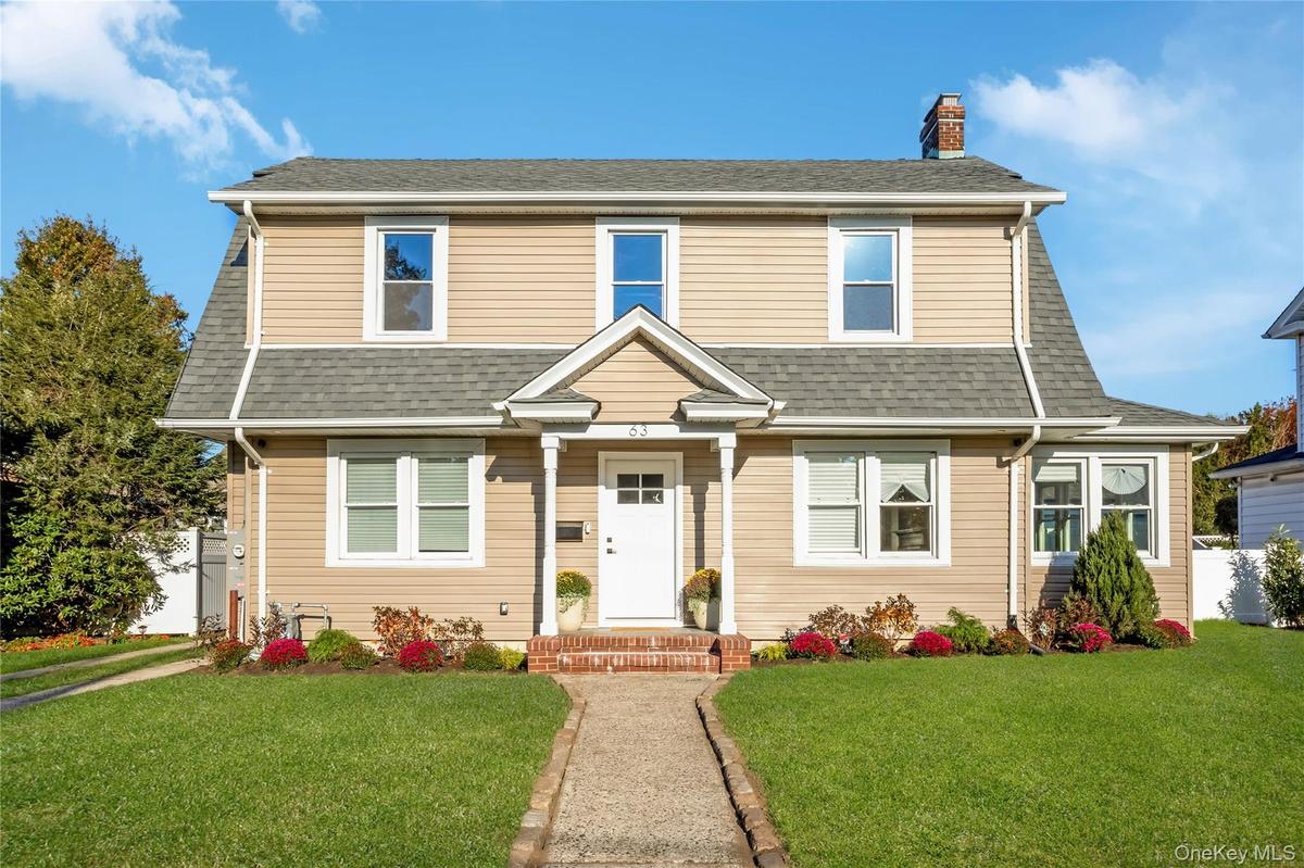 Two-story residence featuring light-toned horizontal siding, a central covered entryway with gable roof detail, a brick-stepped stoop, and an asphalt 