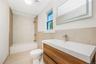 Upstairs full bathroom featuring a floating wood-finish vanity with a rectangular sink, wall-mounted illuminated mirror, neutral wall tiling, and a bu