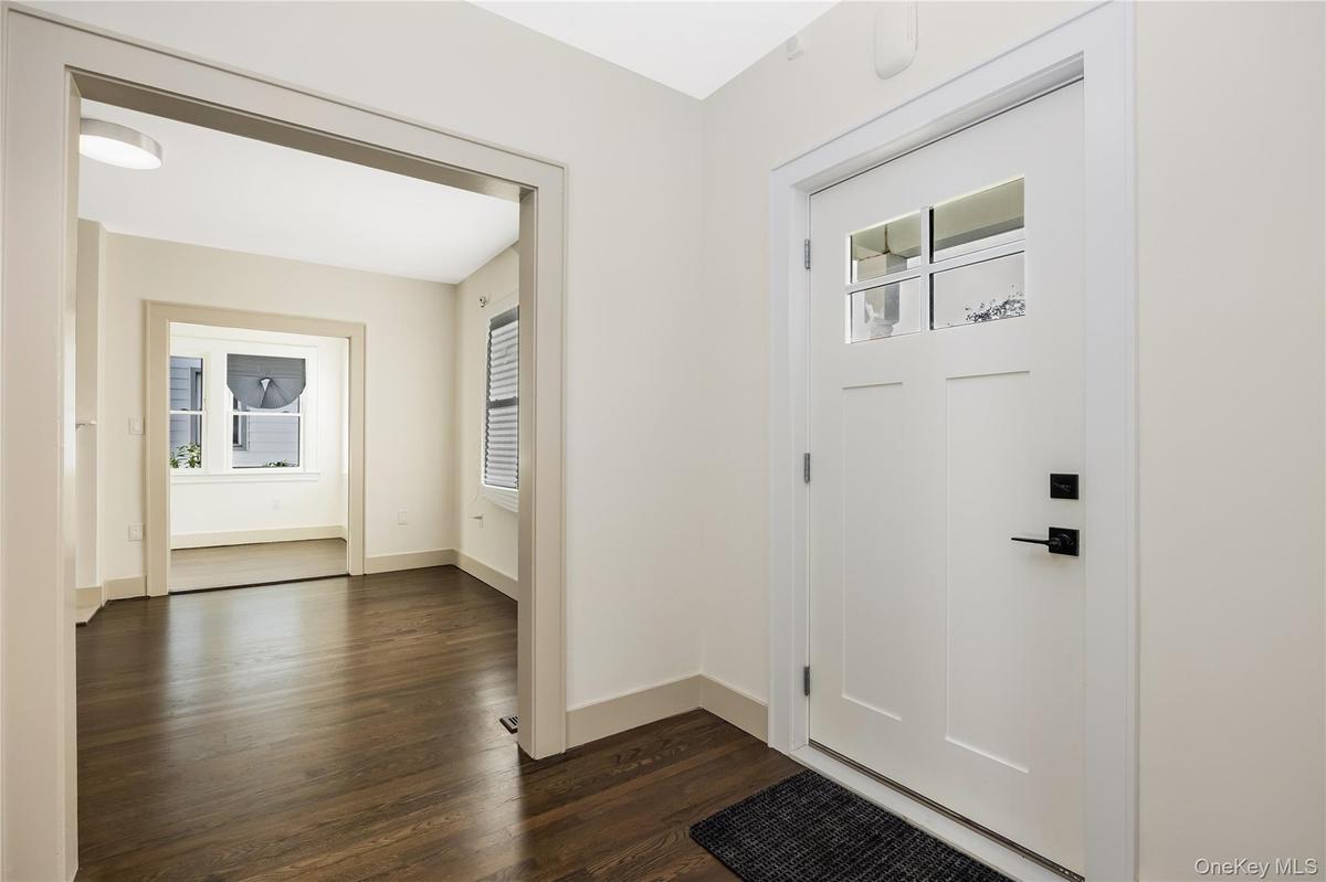 Entryway featuring a white door with glass inlay, matte black hardware, and dark wood-finish flooring