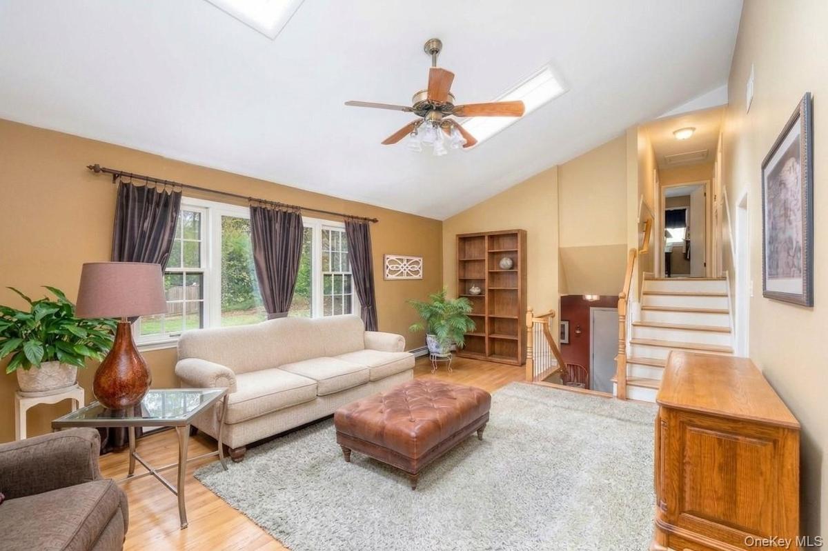Living area featuring a vaulted ceiling, skylight, wood flooring, and multiple windows for natural lighting