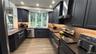 Kitchen featuring dark cabinetry, stone countertops, stainless steel appliances, wood-finish flooring, and a bay window