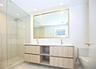 Floating double-vanity with light wood-finish cabinetry, stone-surfaced countertop, glass-enclosed shower with tiled walls, and brass-finish fixtures 