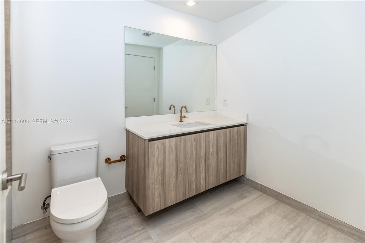 Floating vanity with wood-finish cabinetry, solid-surface countertop, rectangular integrated sink, wall-mounted bronze-tone faucet, and floor-to-ceili