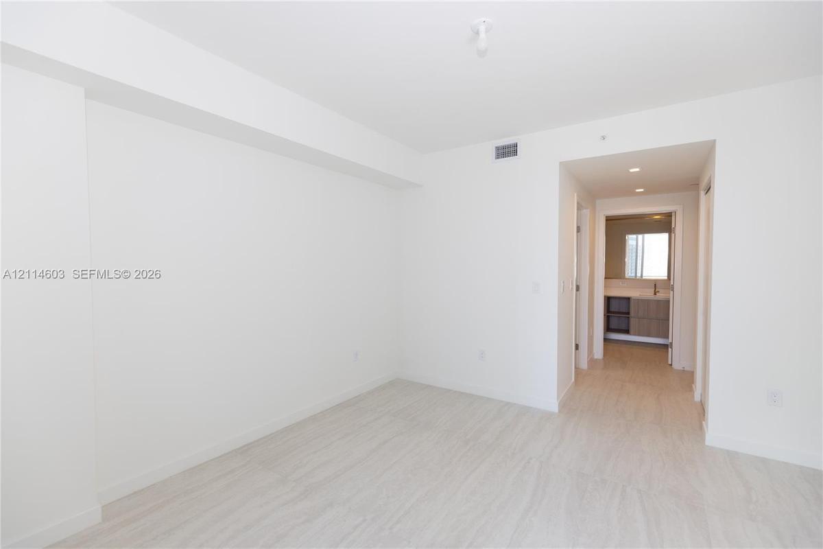 Neutral interior with light-toned wood-finish flooring, smooth white walls, recessed ceiling lighting, and a doorway showcasing a multi-drawer vanity