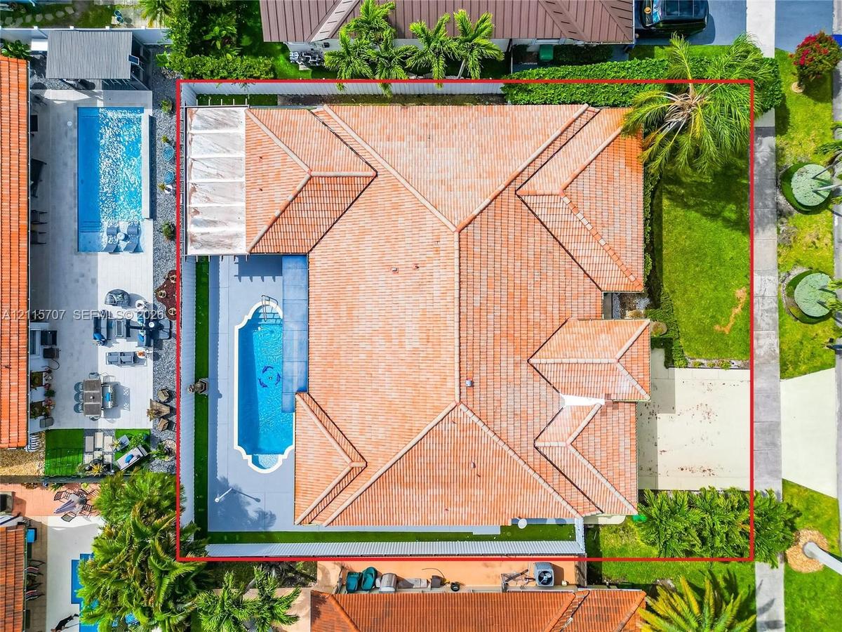 Aerial perspective of a residential property featuring a tiled roof, an in-ground swimming pool with an integrated spa, a concrete pool deck, and a fe