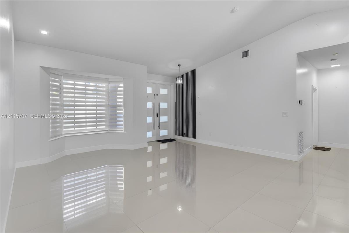 Bright interior featuring vaulted ceilings, polished tile flooring, a multi-pane front entry door with vertical handle hardware, and a bay window equi
