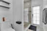 Full-height glass-enclosed shower, wall-mounted matte black shelving, matte black wall-mounted toilet paper holder, and a glass-paneled exterior door
