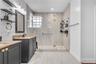 Bathroom featuring a dark wood-finish vanity with stone-surfaced countertop, walk-in shower with floor-to-ceiling tile, glass enclosure, and glass blo