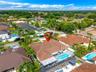 Aerial perspective of a property featuring a tile roof, an in-ground swimming pool, a paved patio area, and mature palm trees