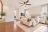 Bedroom featuring wood-finish flooring, a textured geometric accent wall, a central ceiling fan with integrated lighting, and dual windows with layere