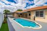 In-ground swimming pool with a custom-shaped perimeter, terra cotta tile roof, retractable fabric awning, wooden-frame pergola, and synthetic turf law