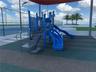 Playground structure featuring multiple slides and integrated staircases set on a rubberized surface, covered by a permanent overhead canopy, with an 