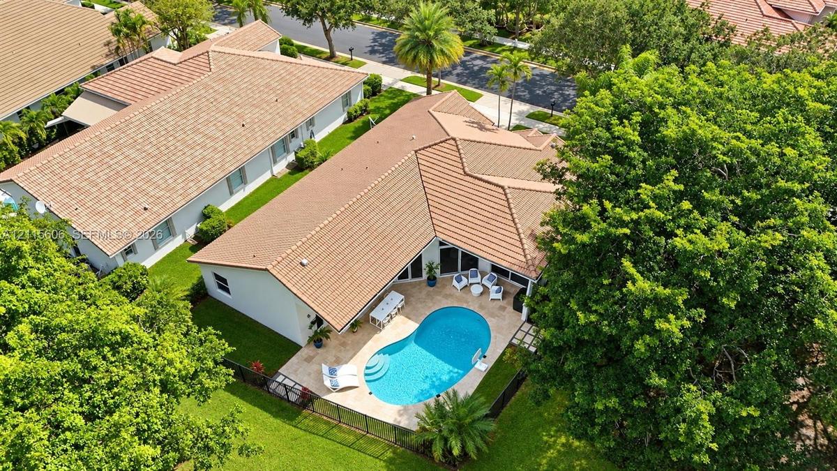 Aerial perspective of a residence featuring a clay tile roof, a private swimming pool with built-in entry steps, a stone-paved patio, and a fenced yar