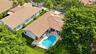Aerial perspective of a residence featuring a clay tile roof, a private swimming pool with built-in entry steps, a stone-paved patio, and a fenced yar