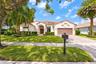 Stucco exterior featuring a clay tile roof, arched entryway, paved driveway, and mature landscaping