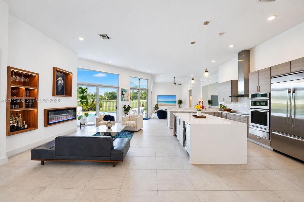 Open-concept living space featuring a central kitchen island with waterfall-edge stone countertop, built-in recessed shelving, integrated linear firep