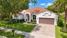 Stucco exterior featuring a red tile roof, arched entryway, paved driveway, and curated landscaping