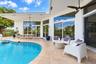 Covered patio featuring stone-tile flooring, ceiling fans, oversized glass sliding doors, and a curved swimming pool