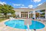Outdoor patio featuring a travertine stone deck, a curved swimming pool with integrated steps, multiple floor-to-ceiling glass sliding doors, and a co