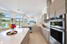 Kitchen featuring a large central island with a quartz countertop, wood-finish cabinetry, stainless steel double wall ovens, a white subway tile backs