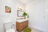 Wood-finish vanity with a rectangular sink, multi-tone glass tile backsplash, framed wall mirror, and chrome multi-bulb light fixture