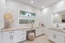 Stacked stone accent wall featuring dual horizontal windows, custom white cabinetry, stone-finish countertops, and a rectangular vessel sink with a wa