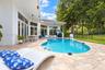 Outdoor patio featuring natural stone pavers, a custom-shaped swimming pool with integrated steps, a covered lanai with ceiling fans, and black metal 