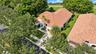 Tile roof architecture, paver driveway, manicured landscaping, and mature trees on a corner lot
