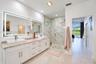 Dual-sink vanity with rectangular vessel basins, stone countertop, large LED-backlit mirror, and glass-enclosed shower with tiled wall surfacing
