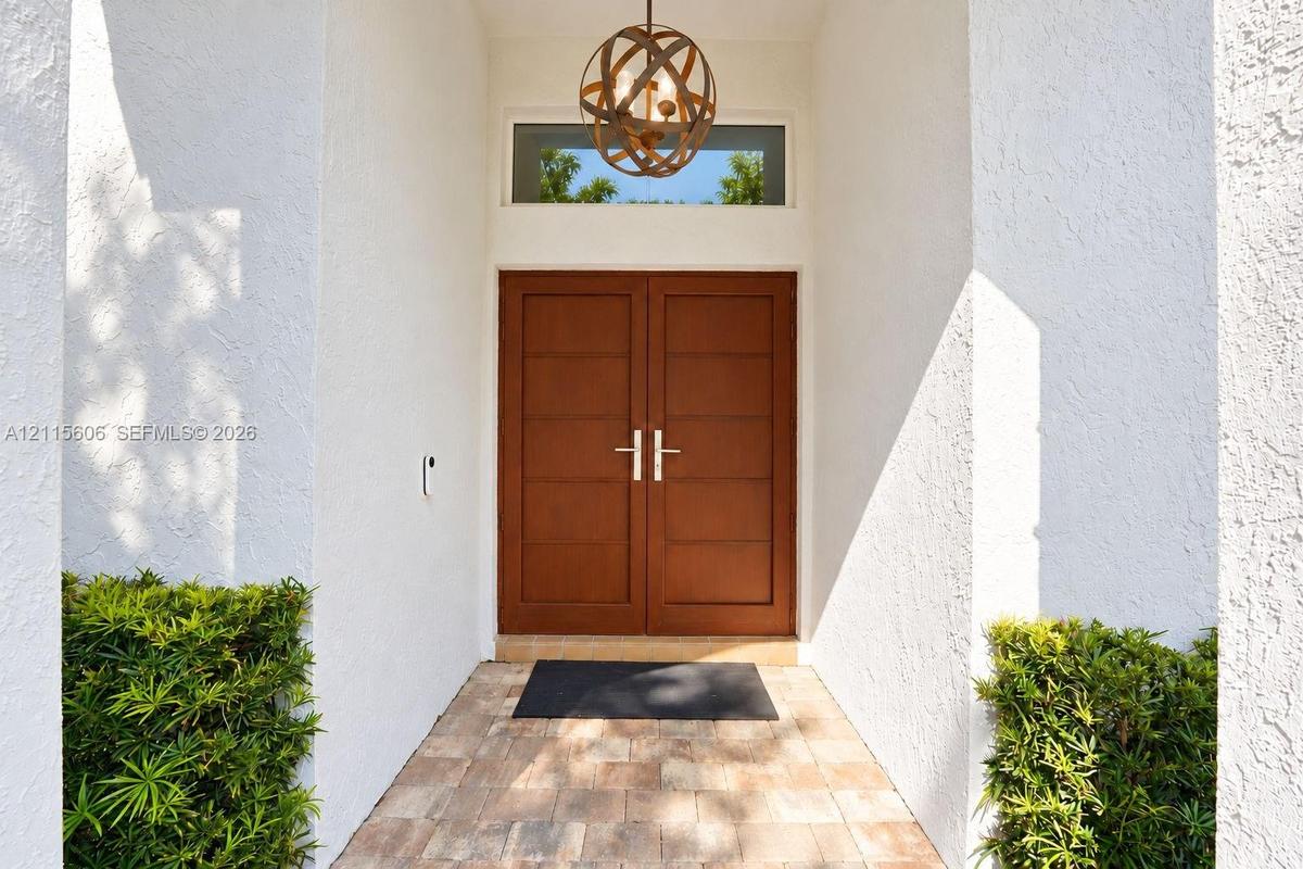 Entryway featuring double wood-finish doors with horizontal paneling, a circular metal orb pendant light fixture, a rectangular transom window, and st