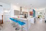 Kitchen featuring flat-panel cabinetry, a quartz-topped island with waterfall edge, stainless steel appliances, a white subway tile backsplash, and ov