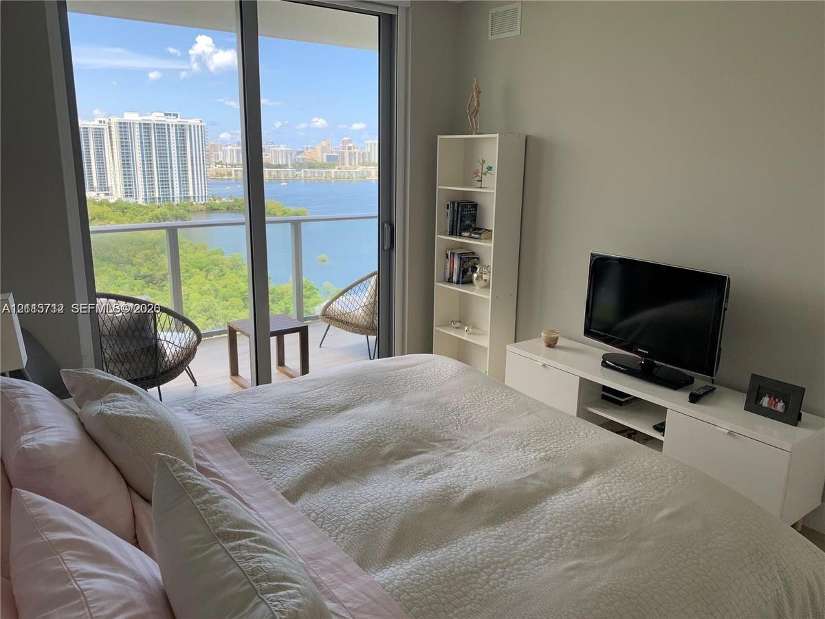 Floor-to-ceiling glass sliding doors opening to a private balcony with metal railing, floor-to-ceiling windows, and expansive waterfront scenery