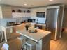 Modern kitchen featuring wood-finish cabinetry, white solid-surface countertops, a center island with bar seating, stainless steel appliances, and int