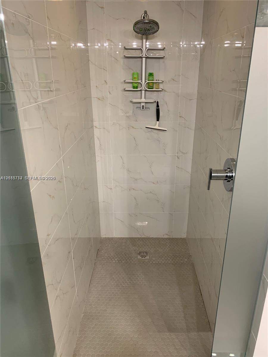 Walk-in shower featuring floor-to-ceiling large-format tile with marble-pattern veining, textured mosaic tile flooring, a wall-mounted rainfall shower