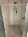 Walk-in shower featuring floor-to-ceiling large-format tile with marble-pattern veining, textured mosaic tile flooring, a wall-mounted rainfall shower