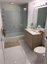 Bathroom featuring a wood-finish vanity, solid-surface countertop with integrated sink, glass-enclosed shower and tub combination with tile surround, 